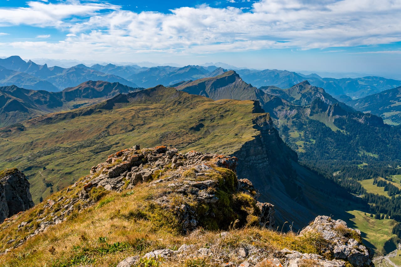Ein weites Berglandschaftspanorama mit grünen Hügeln, schroffen Felsformationen und tiefen Tälern.