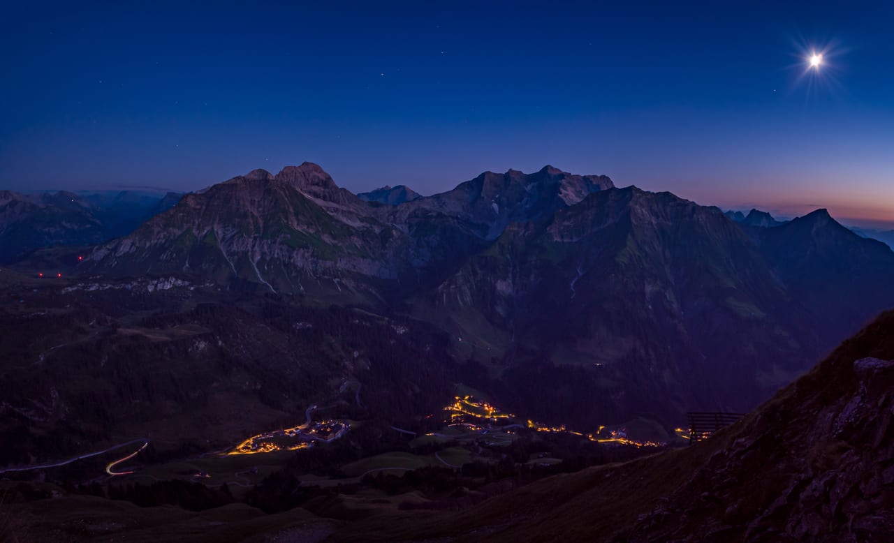 Ein nächtliches Bergpanorama mit schneebedeckten Gipfeln, die im sanften Mondlicht und zarten Dämmerungshimmel erstrahlen.