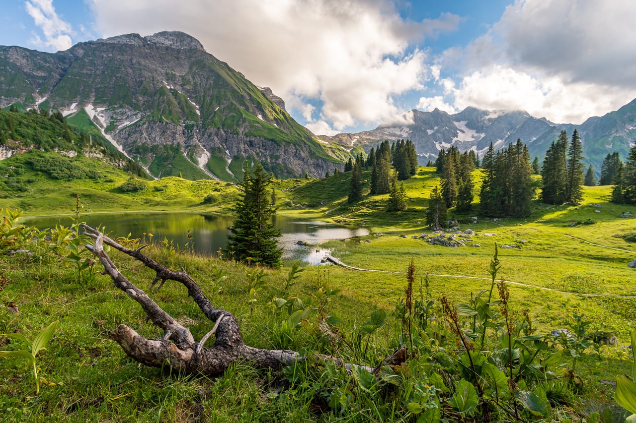 Ein ruhiger Bergsee spiegelt die umliegenden grünen Hügel und schneebedeckten Gipfel der Alpen wider.