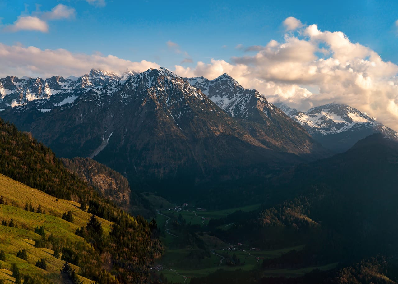 Eine Berglandschaft der Alpen mit schneebedeckten Gipfeln, grünen Tälern und bewölktem Himmel.