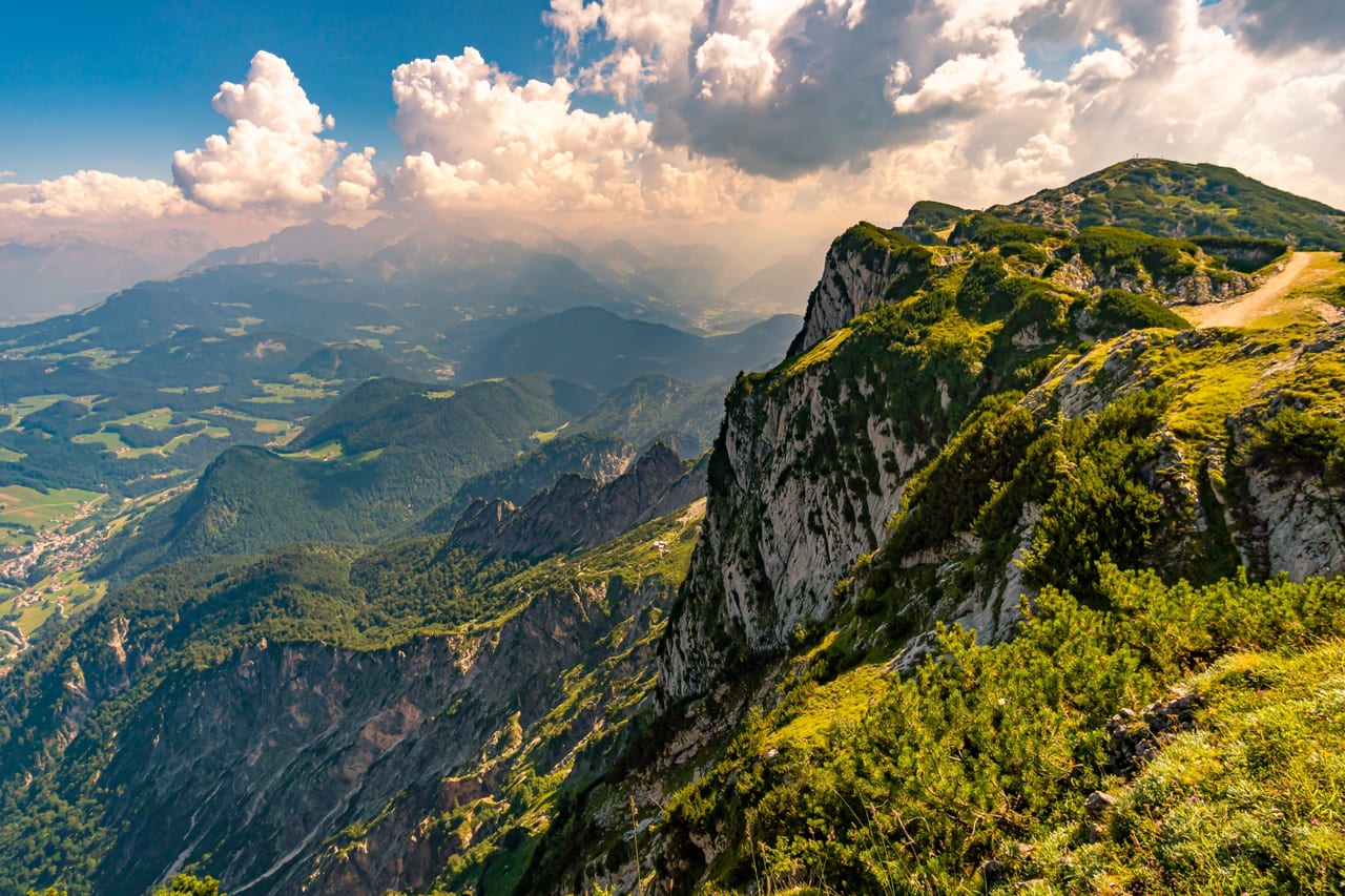 Eine steile, grüne Felsformation in den Alpen mit üppiger Vegetation, die sich in die Tiefe erstreckt.