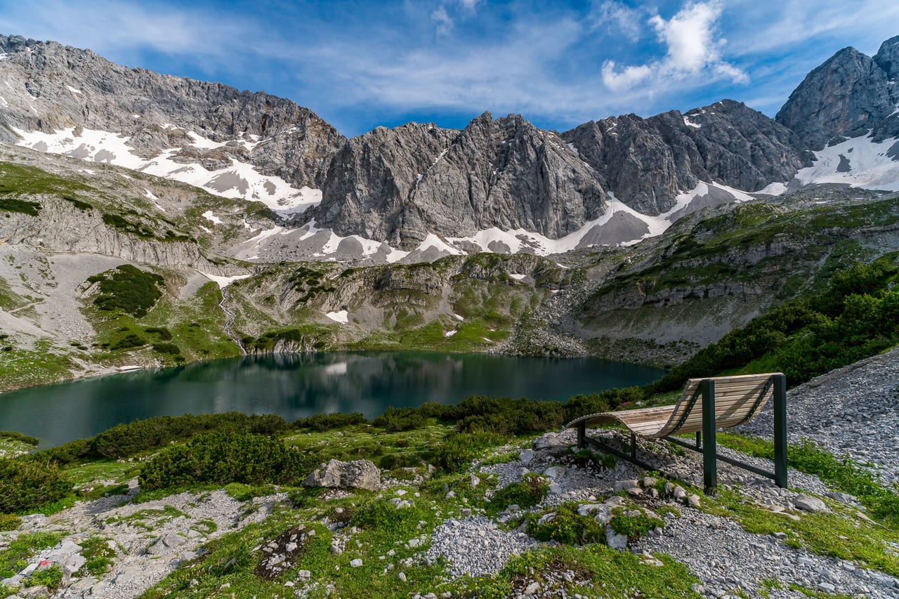 Ein klarer Bergsee liegt eingebettet zwischen schroffen Felsformationen und schneebedeckten Gipfeln.