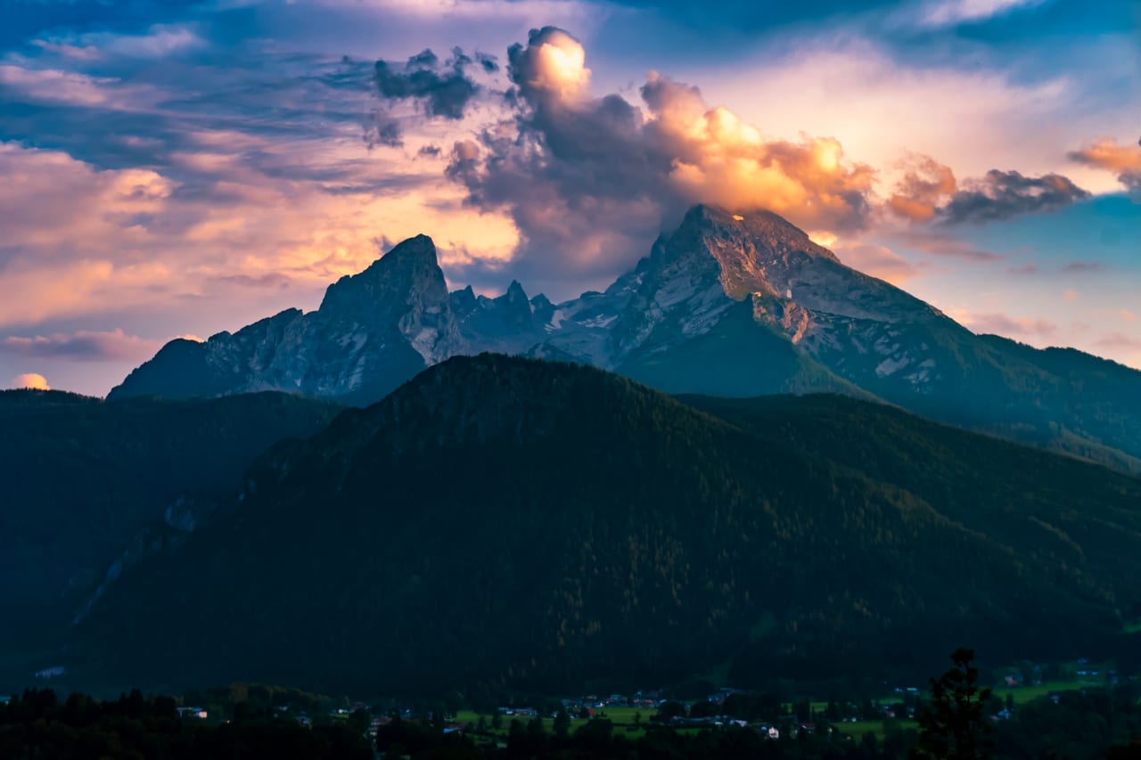 Eine majestätische Bergformation der Alpen bei Sonnenuntergang, deren Gipfel in warmen Orangetönen leuchten.