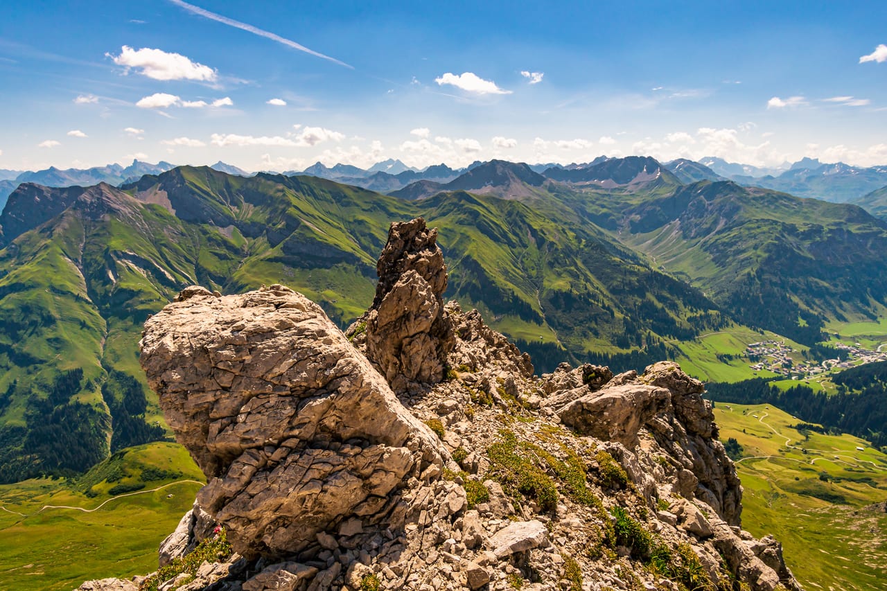 Eine weite Berglandschaft der Alpen mit grünen Tälern und schroffen Felsformationen im Vordergrund.