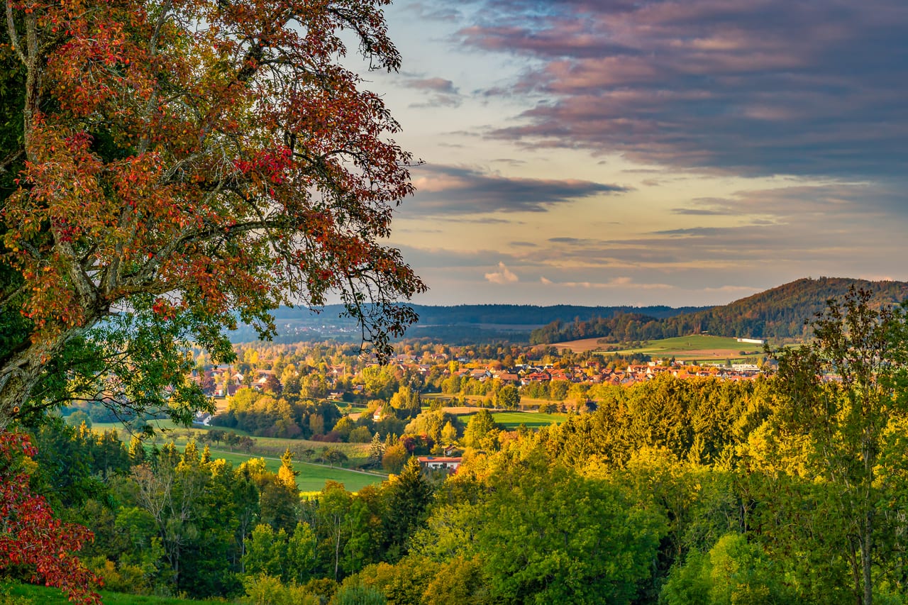 Eine malerische Panoramaaufnahme eines kleinen Dorfes in einer hügeligen Landschaft während des Sonnenuntergangs.