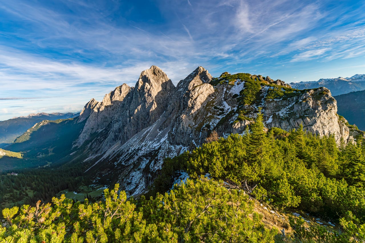 Ein majestätisches Bergmassiv mit steilen, schneebedeckten Felsformationen und grünen Kiefernwäldern im Vordergrund.