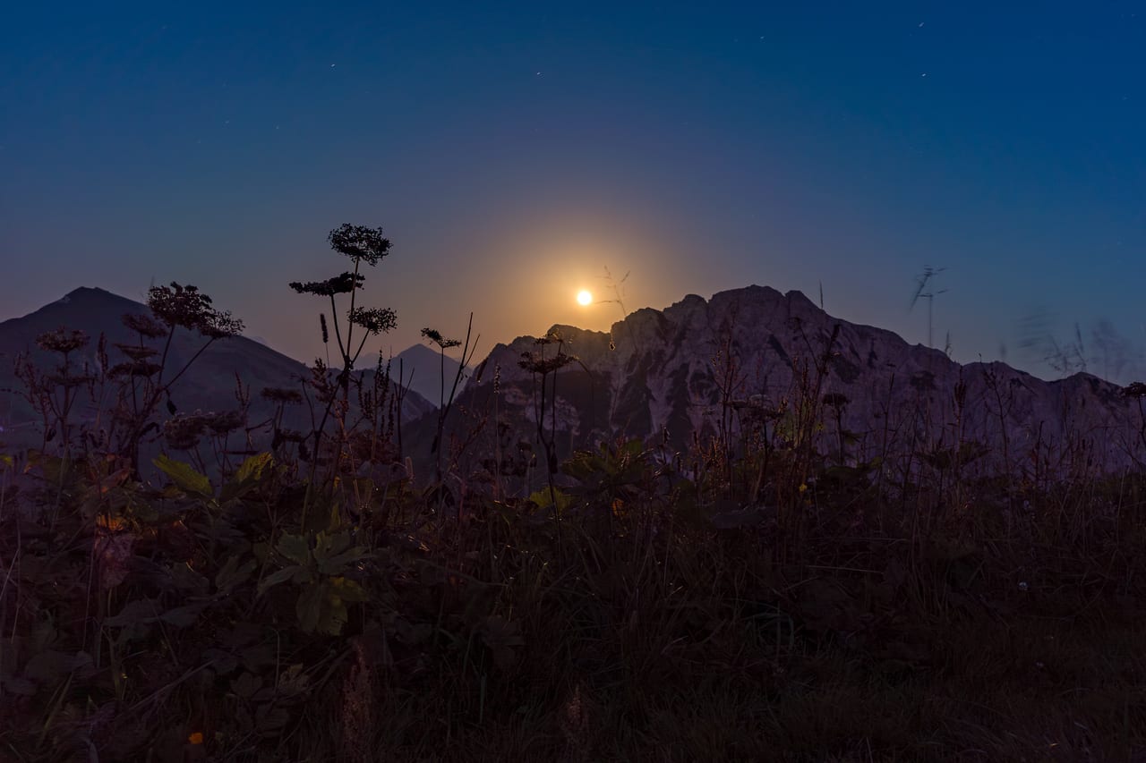 Ein goldener Mond steigt hinter schroffen Felsformationen und Nebelschwaden auf.