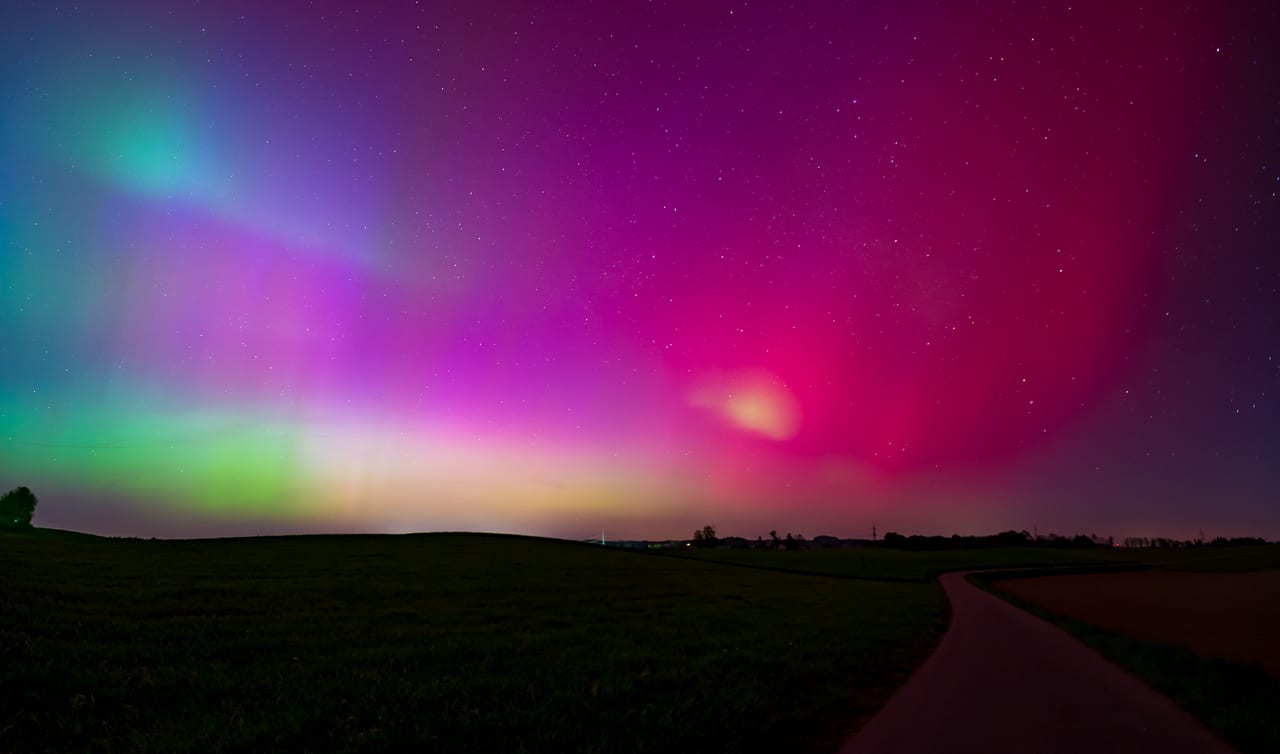Eine nächtliche Landschaft mit einer leuchtenden Aurora borealis in Grün-, Pink- und Violetttönen über einem dunklen Feld.