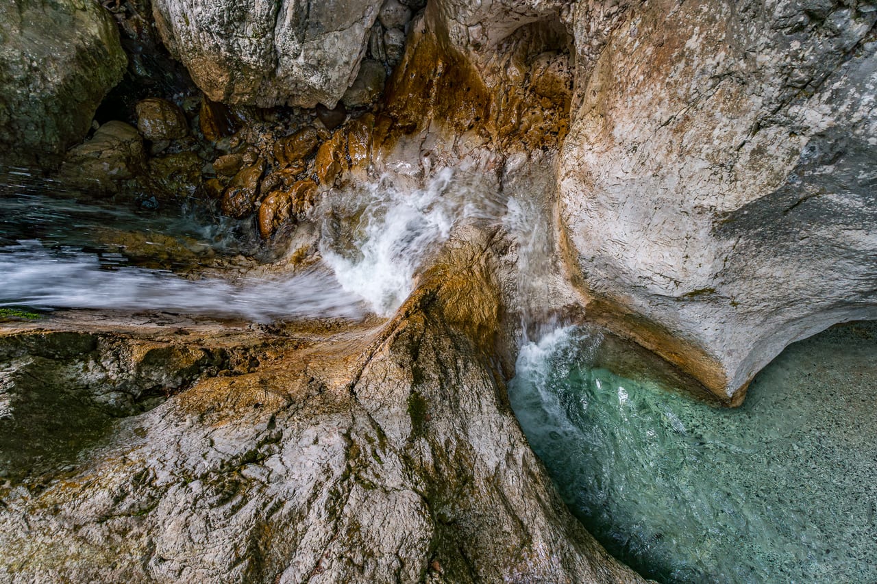 Ein schmaler Wasserstrom stürzt über moosbewachsene Felsplatten in ein klares, türkisfarbenes Becken.