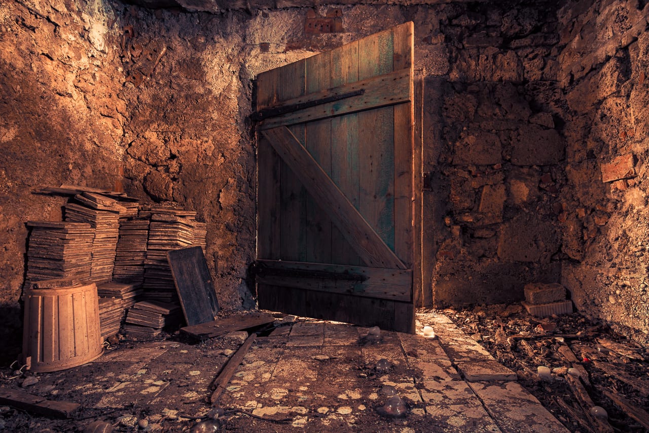 Eine verlassene, moosbewachsene und von Schutt übersehte Kammer mit einer alten Holztür.
