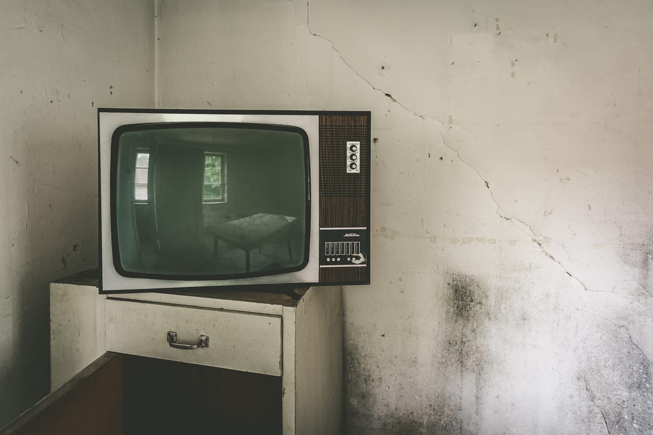 Ein alter Fernseher steht auf einem abgenutzten Möbelstück in einer verlassenen, verwitterten Zimmer.