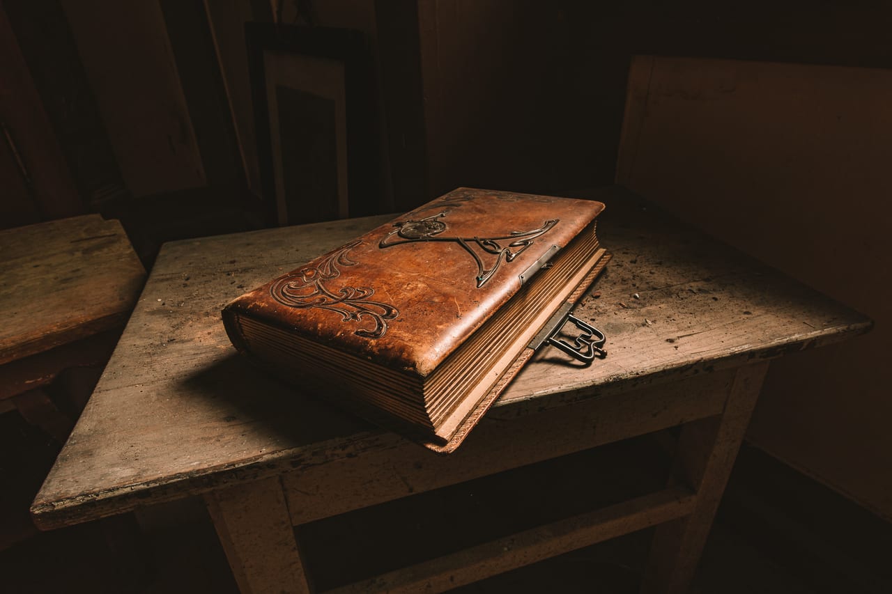 Ein antikes Buch, mit Ornamenten verzierter Ledercover liegt auf einem verwitterten Holztisch.