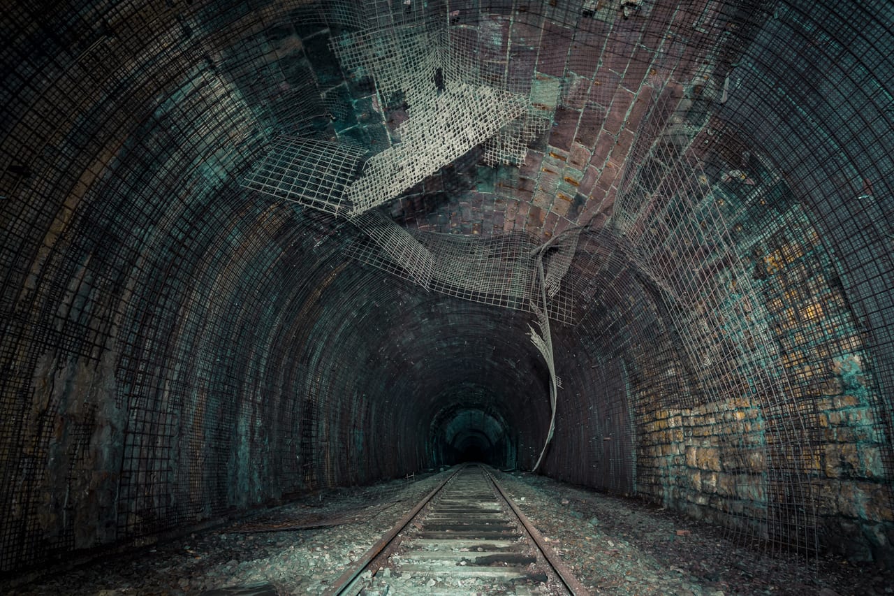 Ein verlassener Tunnel mit abgewetzten Betonwänden, die durch Metallgitter verstärkt sind.