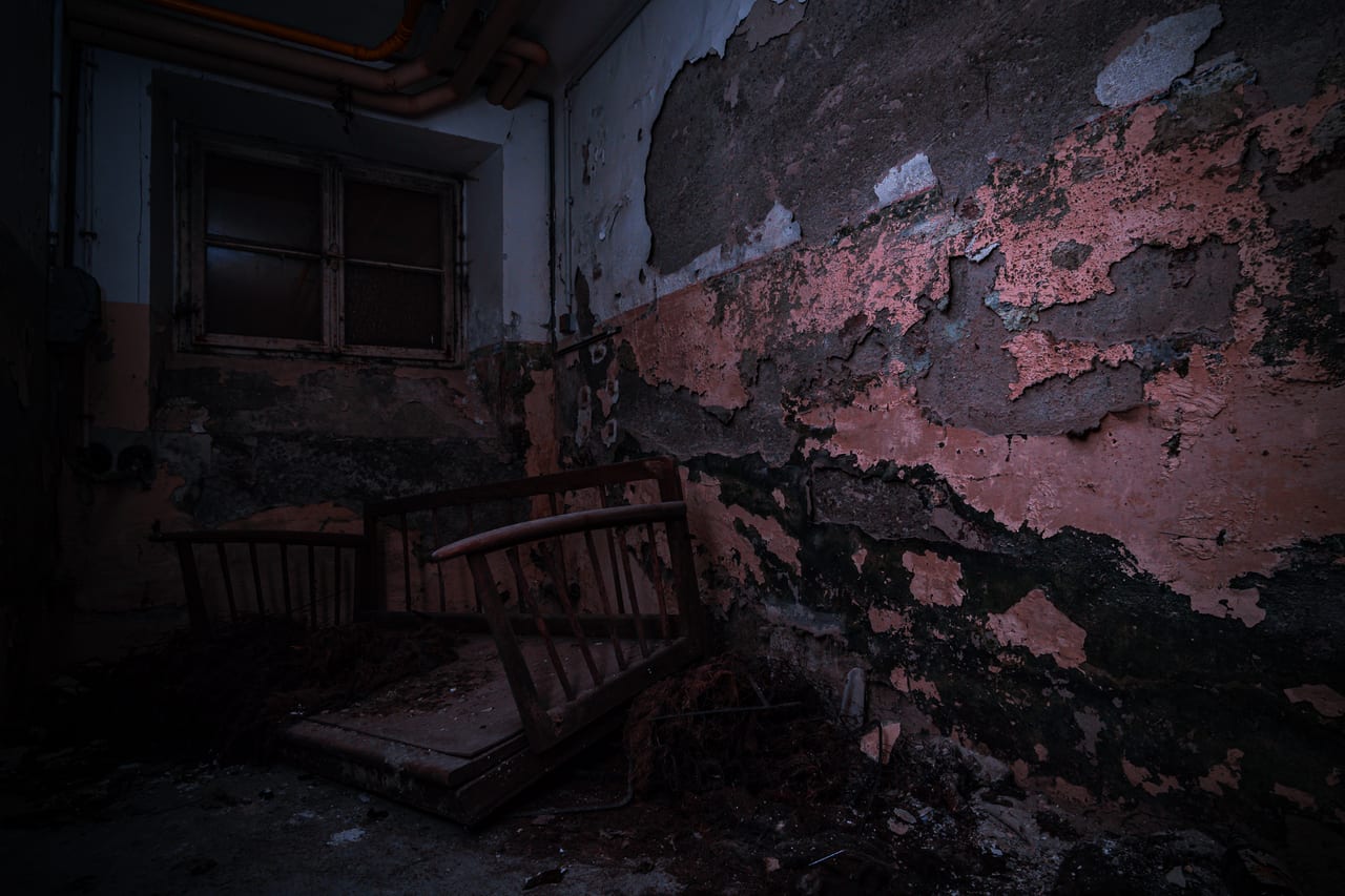 Ein verlassener Raum mit stark beschädigten, abblätternden Wänden und einer heruntergekommenen, dunklen Holzbank.