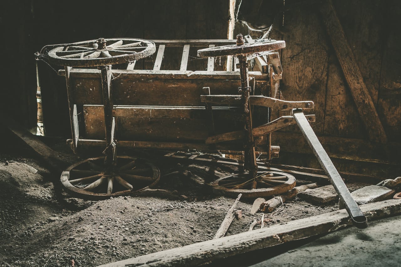 Eine alte, verfallene Förderkarre mit zwei großen Holzrädern und Metallgestell steht auf einem schmutzigen Boden.