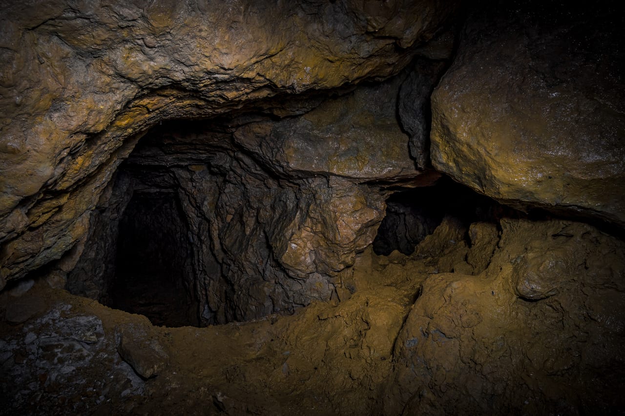 Düstere, moosbewachsene und von Wasser geformte Felswände eines verlassenen Bergwerks mit markanten Schichtungen.