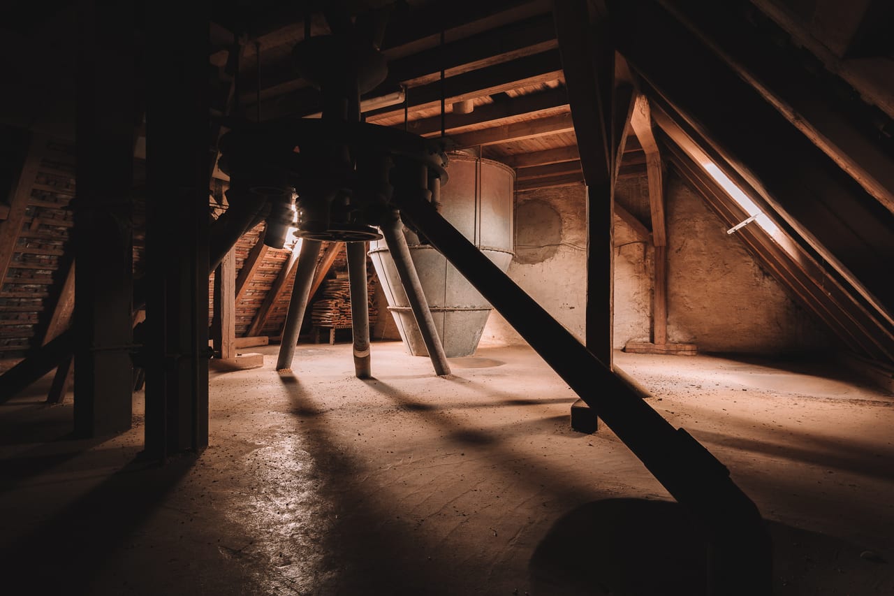 Verlassene Mühle mit sichtbaren Stahlträgern und Betonböden, durch die ein schmaler Lichtstrahl von oben einfällt.