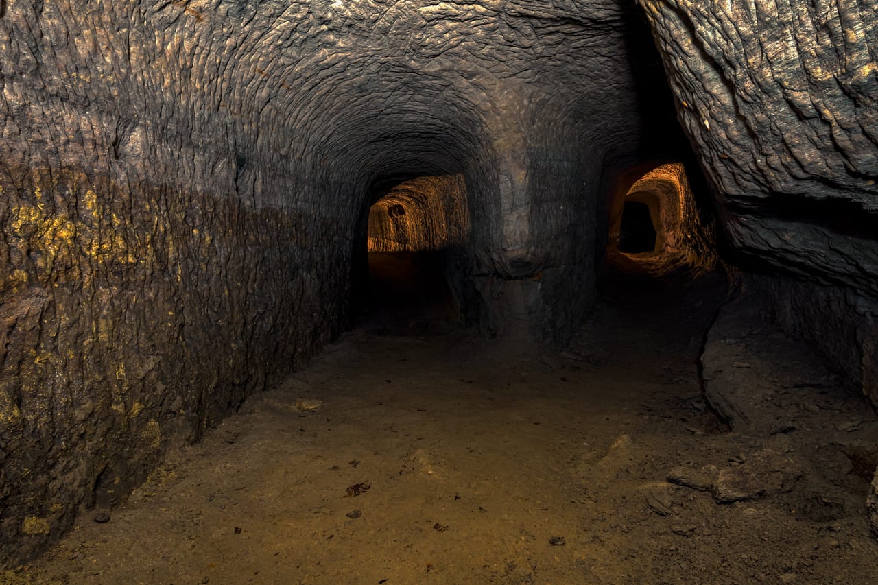 Dunkler, verlassener Tunnel mit unebenen Wänden und zwei seitlichen Öffnungen, die in weitere Gänge führen.