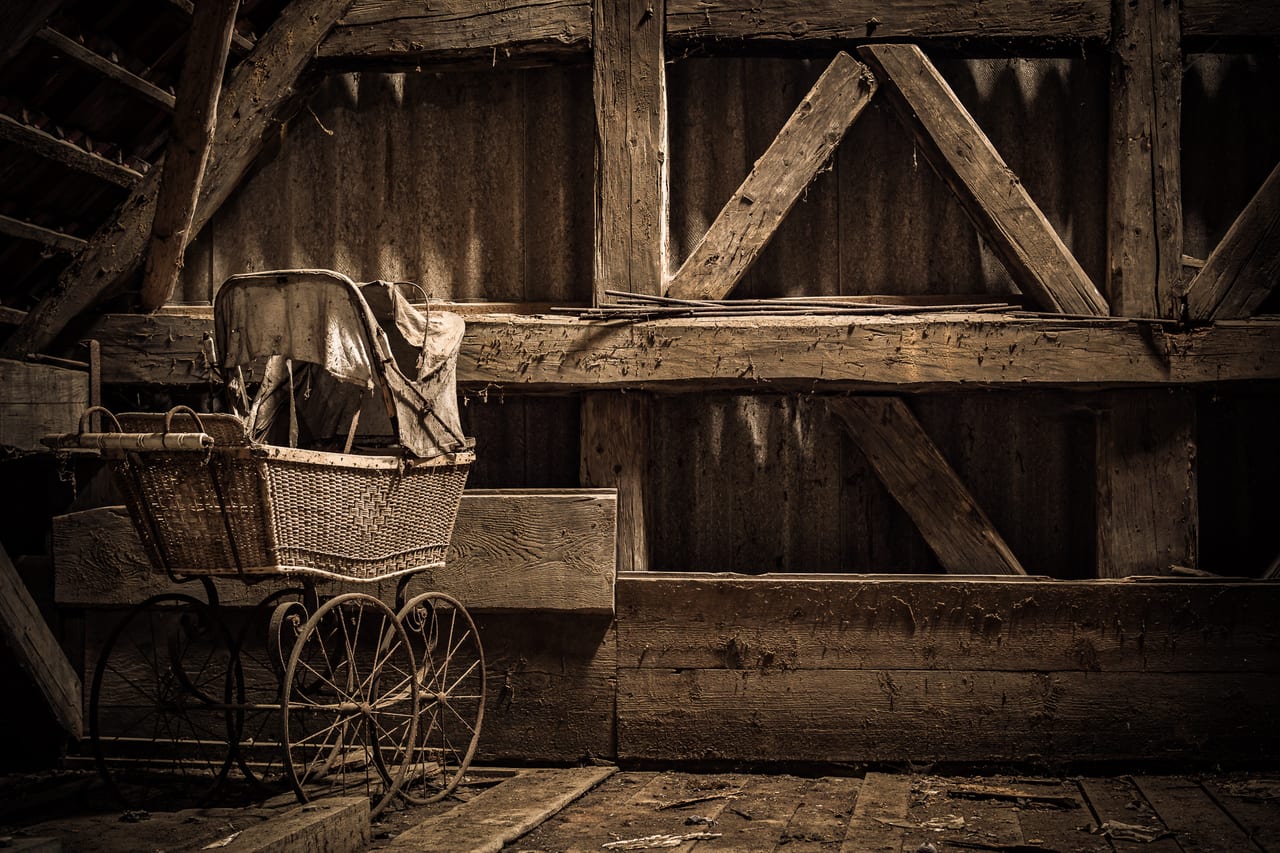 Ein rostiger Kinderwagen steht auf einem verwitterten Holzpodest in einer verlassenen Scheune.