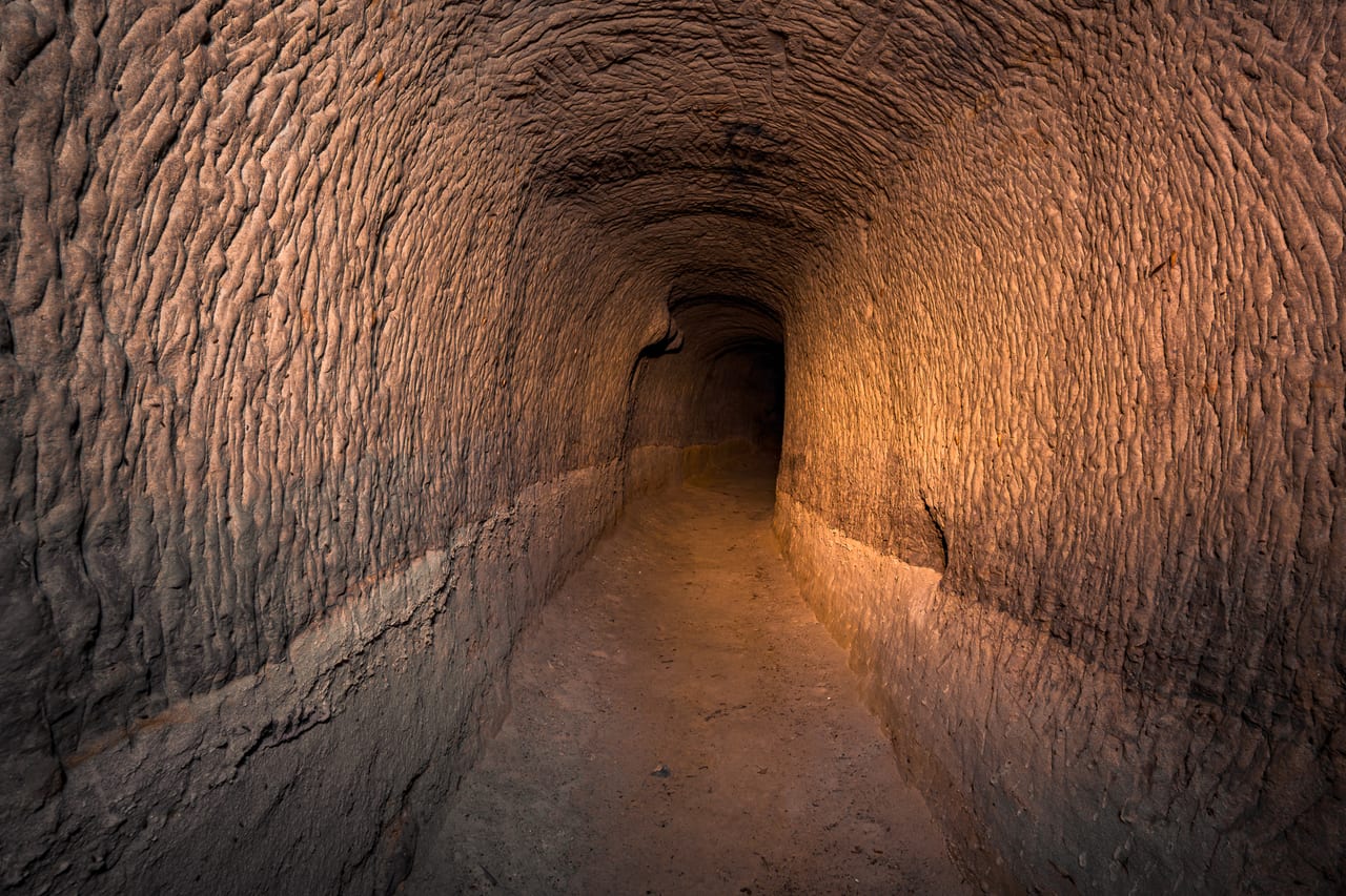 Ein langer, gewölbter Tunnel aus grob behauenen Steinblöcken, der in der Ferne in ein helles Licht übergeht.