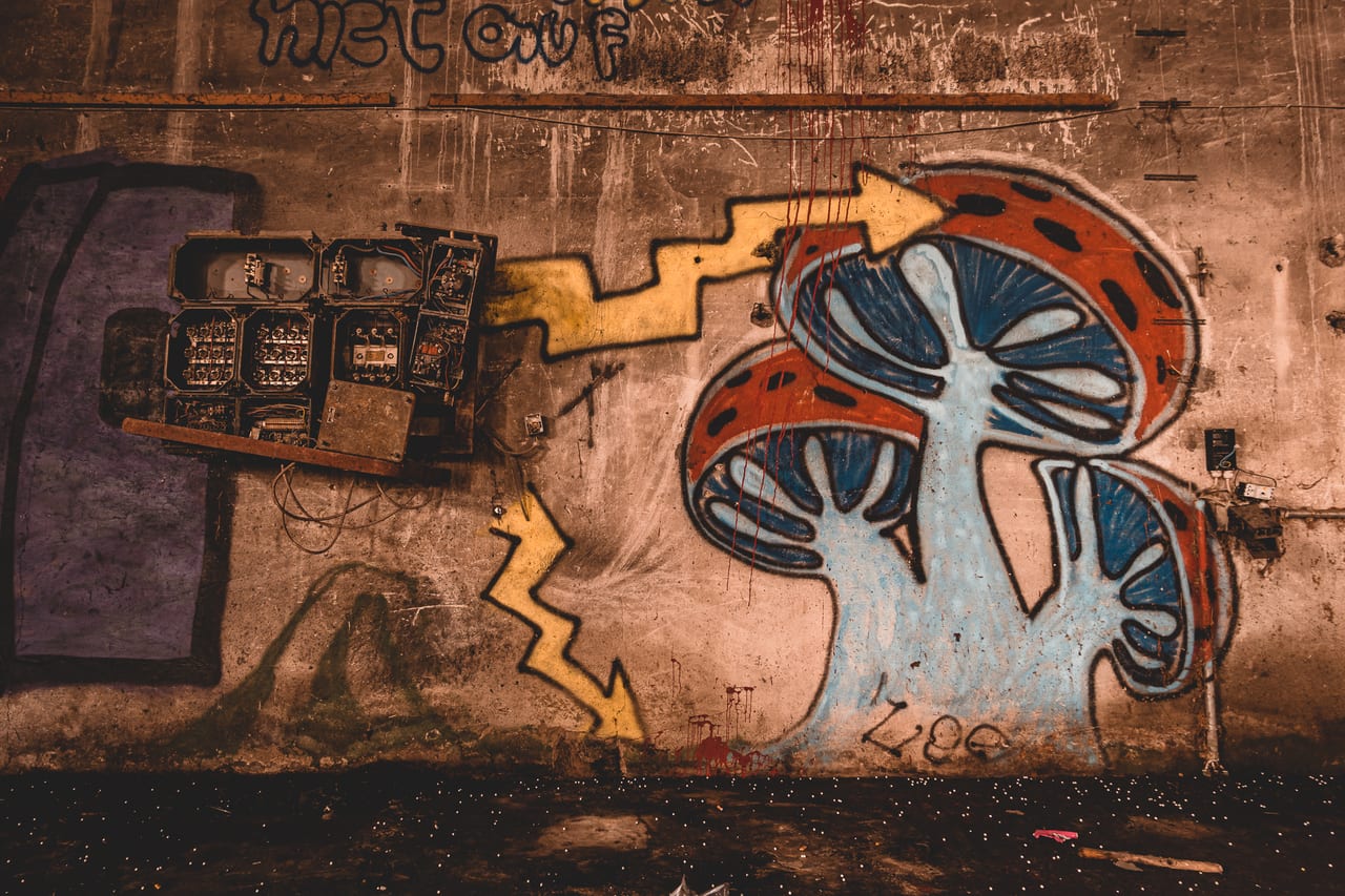 Eine verwitterte Wand mit altertümlichen Elektroinstallationen und einem großen, abstrakten Graffiti-Motiv.