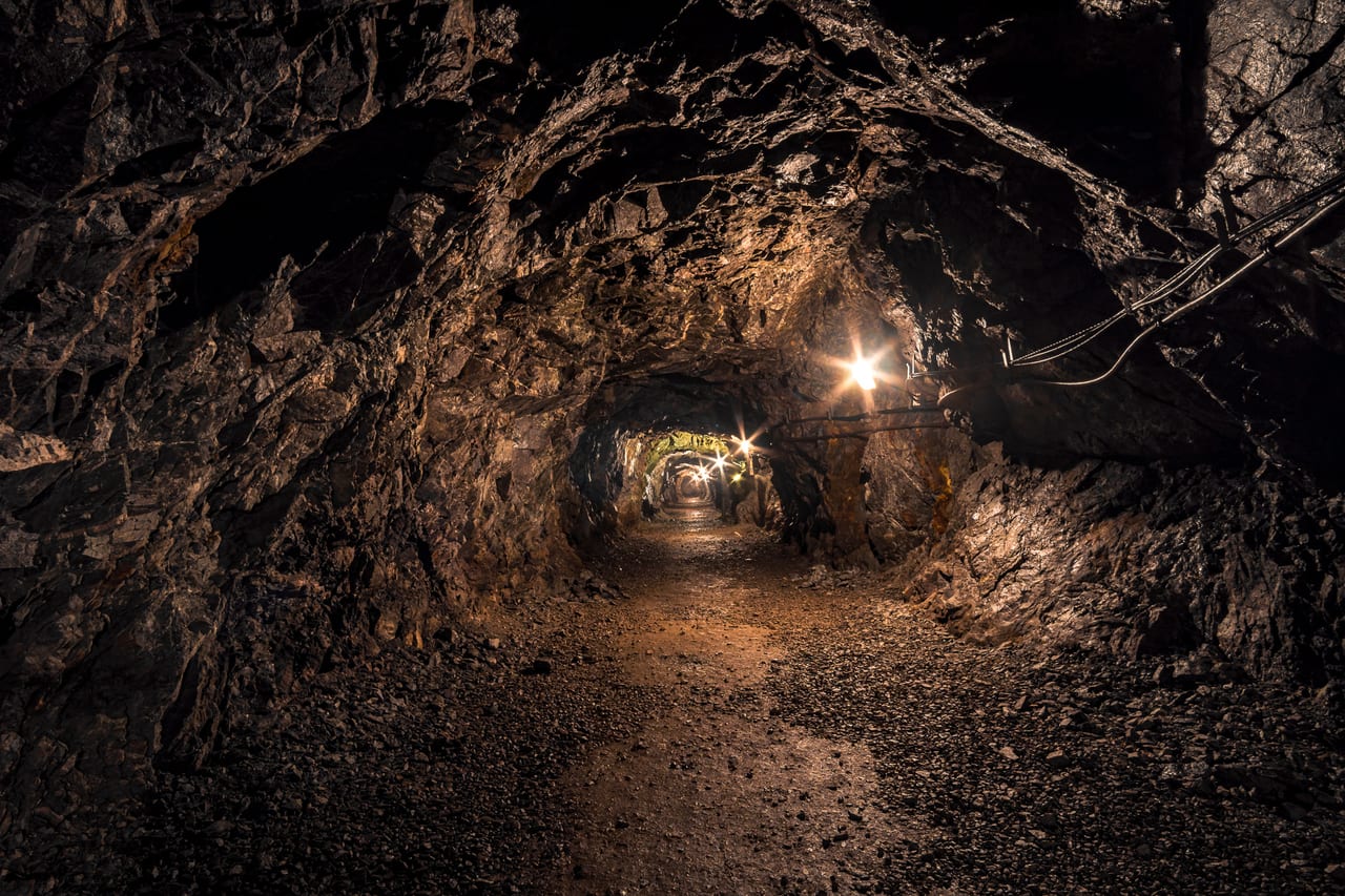Ein dunkler, verlassener Tunnel in einem alten Bergwerk, der durch künstliches Licht am Ende des Gangs beleuchtet wird.