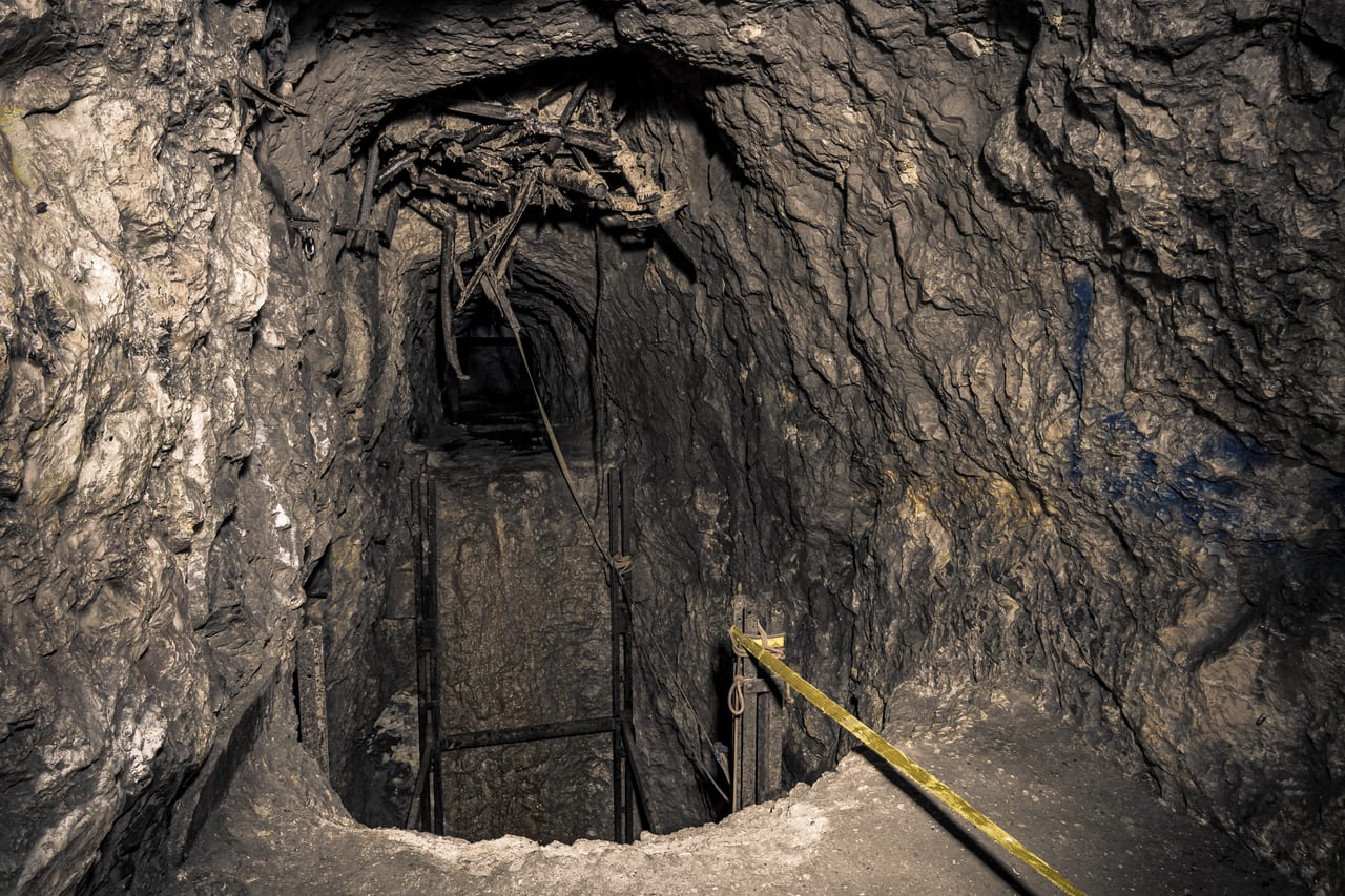 Ein dunkler, verlassener Schachteingang in einem alten Westwall Bunker mit rostigen Metallgittern und Seilen.